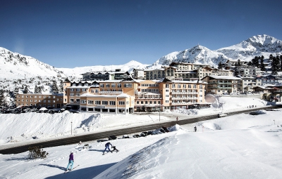 View of the exterior of the 4 star superior Hotel Steiner and the ski resort of Obertauern, Austria, with snow covered piste, panoramic mountain scenery and blue skies