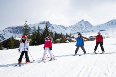 Children skiing on gentle ski slope in Courchevel, France with mountain scenery and chalet-style buildings - Snow-wise - Ski February Half Term 2023 - Luxury tailor-made ski holidays to luxury family ski hotels across the Alps