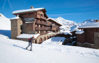 View of skier on snow-covered piste next to the chalet-style exterior of the 5 star hotel Les Suites du Montana in the ski-resort of Tignes, France