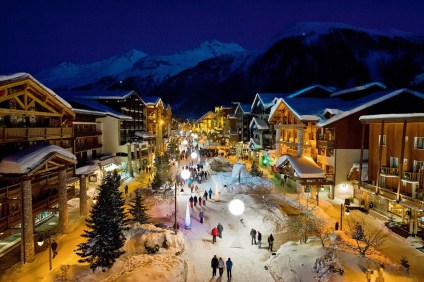 Snow-covered streets and illuminated chalet-style buildings in Val d'Isère on a winter evening