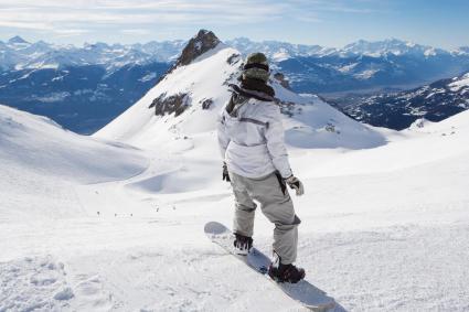 Snowboarder overlooking snow-covered mountain peaks and glacier slopes high in the Alps