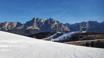 Snow-covered ski piste in the Dolomites with largely snow-free mountainsides in the background